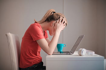 Young woman feeling stressed while studying at home with a laptop and coffee cup. HD wallpaper