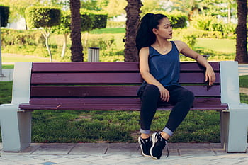A young woman sits on a bench in a sunny park, enjoying a moment of relaxation. HD wallpaper