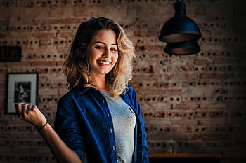 Portrait of a smiling woman in denim jacket against a brick wall indoors. HD wallpaper