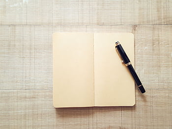 Minimalist top-view of an open notebook with a pen on a wooden surface for writing inspiration. HD wallpaper