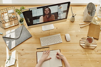 Person taking notes during a video call at a neatly organized home desk, showing remote work lifestyle. HD wallpaper