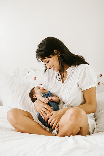 A mother lovingly cradles her baby in a serene bedroom setting. HD phone wallpaper