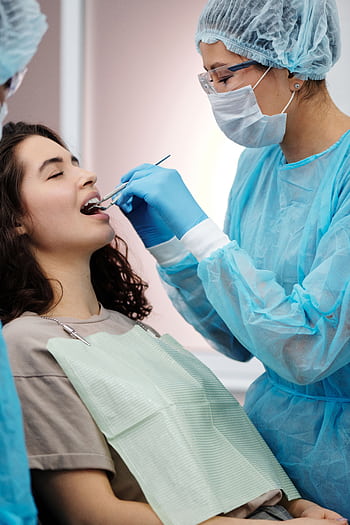 Dentist in protective gear examining a woman's teeth during a dental clinic visit. HD phone wallpaper