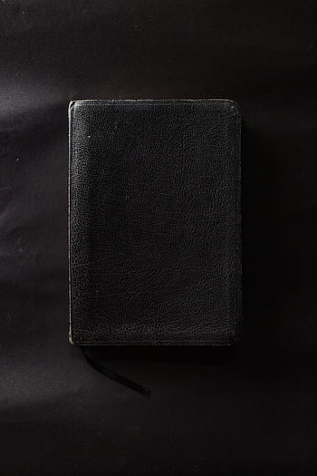 A closed black leather-bound book on a plain black surface. HD phone wallpaper