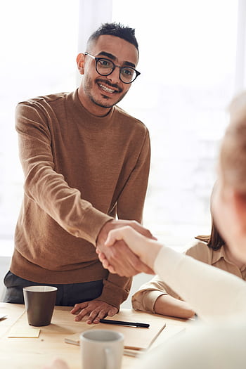 Smiling professionals engage in a welcoming handshake at a business meeting indoors. HD phone wallpaper