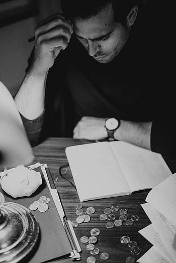 Black and white of a man contemplating finances at a desk with coins and notebook. HD phone wallpaper