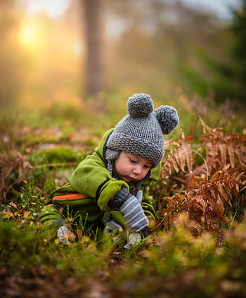 A cute baby in a knit hat and green outfit exploring nature during sunset. HD phone wallpaper