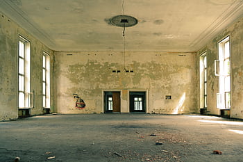 A spacious abandoned room with graffiti, peeling walls, and natural light streaming through large windows. HD wallpaper