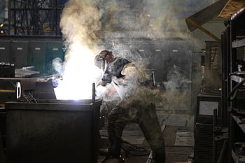 A skilled welder working with intense sparks and smoke in an industrial workshop, showcasing safety and precision. HD wallpaper