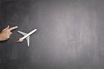 Conceptual of a hand pointing towards a toy plane on a chalkboard background, symbolizing travel and direction. HD wallpaper