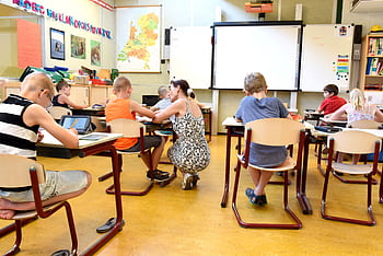 Children engaged in learning with a teacher in a bright classroom setting. HD wallpaper