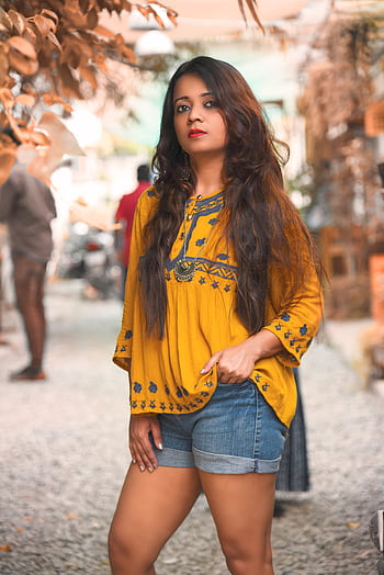 Fashionable woman posing in a vibrant yellow boho top and denim shorts outdoors. HD phone wallpaper