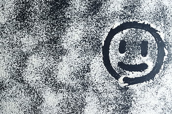 Artistic smiley face drawn through white powder on a black surface, creating an abstract texture. HD wallpaper