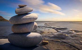 A serene stack of stones on the rocky seashore during a peaceful sunrise, embodying balance and zen. HD wallpaper