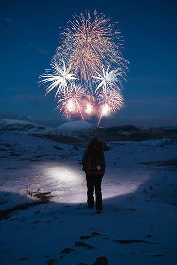 A lone hiker watches fireworks illuminating a snowy winter night, creating a magical outdoor scene. HD phone wallpaper