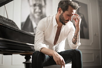 A pensive musician sits beside a piano in an elegant room, reflecting deeply. HD wallpaper