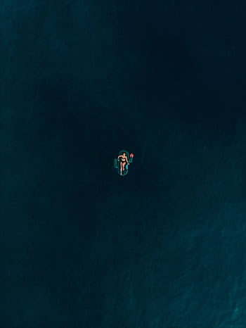 A lone woman on an inflatable float relaxes in the vast blue ocean, creating a serene and peaceful scene. HD phone wallpaper