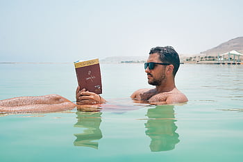 Relaxing man reading a book while floating on the Dead Sea under bright sunlight. HD wallpaper