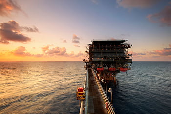 A breathtaking view of an oil platform on the ocean at sunset, showcasing industrial beauty. HD wallpaper