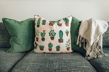 A modern living room with green cushions, cactus pillow, and cozy throw blanket on a sofa. HD wallpaper