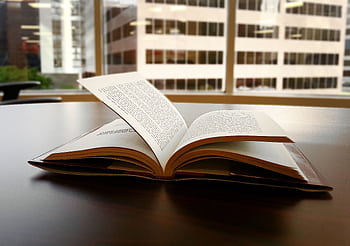 An open book sits on a desk in an office overlooking a city skyline through large windows. HD wallpaper