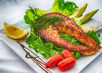 Delicious grilled salmon served with fresh vegetables and herbs on a white plate. HD wallpaper
