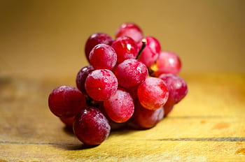 A vibrant bunch of fresh red grapes displayed on a rustic wooden surface. HD wallpaper