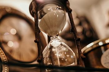 Close-up of a vintage hourglass with blurred antique clock background, evoking a timeless feel. HD wallpaper