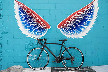 A stylish bicycle parked against a vibrant blue wall with colorful wing graffiti art, creating an urban vibe. HD wallpaper