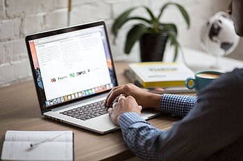 A man working on a laptop at a desk with coffee, showcasing remote work in a modern office setting. HD wallpaper