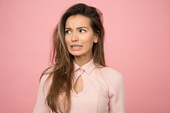 A young woman with a playful uncertain expression against a pink background. HD wallpaper
