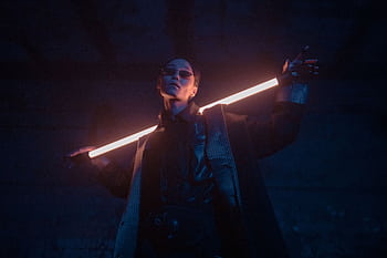 A stylish individual poses with a glowing neon stick in a dark, cyberpunk setting. HD wallpaper