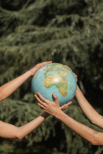 Four hands holding a globe outdoors, symbolizing unity and environmental conservation. HD phone wallpaper