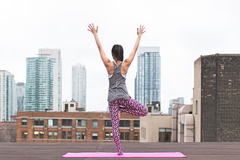 Woman in yoga pose on rooftop with city skyscrapers in the background. HD wallpaper