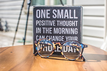 Eyeglasses resting on a table in front of a motivational quote sign, emphasizing positivity. HD wallpaper