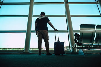 Man with luggage waiting at airport lounge, anticipating departure in a modern setting. HD wallpaper