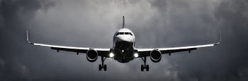 A dramatic view of an airplane landing with stormy clouds overhead, showcasing aviation in a monochrome scene. HD wallpaper