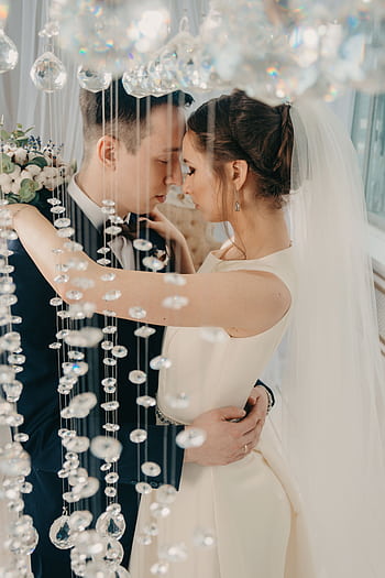 Elegant bride and groom embrace amidst sparkling crystal decor in a romantic indoor setting. HD phone wallpaper