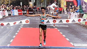 A triumphant marathon winner crosses the finish line, embodying athletic success. HD wallpaper