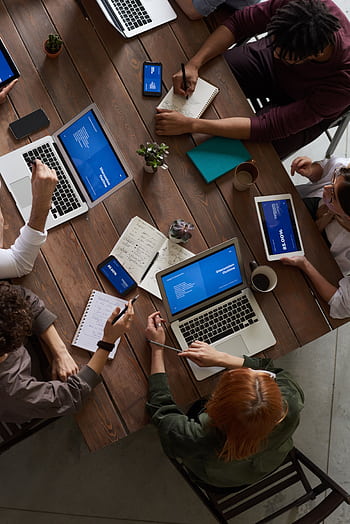 A diverse group of professionals brainstorming with laptops and notepads in a modern office. HD phone wallpaper