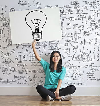 Young woman holds a light bulb drawing against a creative brainstorming wall. HD phone wallpaper