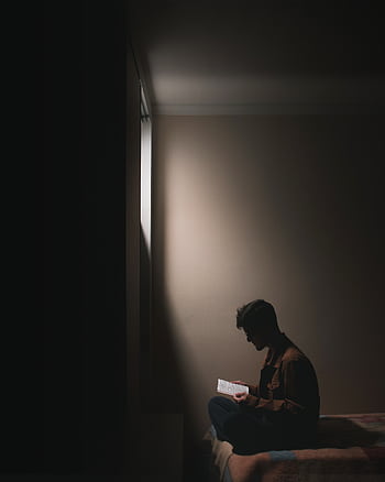 Silhouette of a man sitting on a bed in a dark room, reading a book by window light. HD phone wallpaper