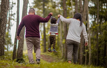 A happy family walking through a forest, lifting their child playfully outdoors. HD wallpaper
