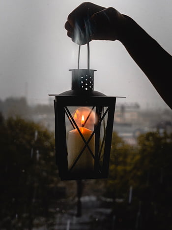 A glowing candle lantern held up against a rainy night backdrop, creating a moody ambiance. HD phone wallpaper