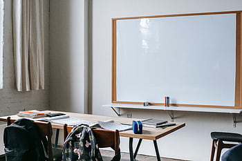 An empty classroom with wooden desks, chairs, and a large whiteboard for teaching. HD wallpaper