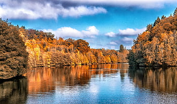 Autumn landscape showcasing vibrant foliage reflected in a calm river. HD wallpaper