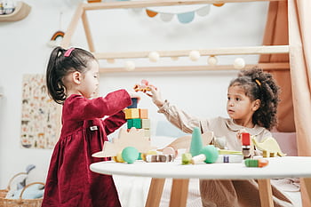 Two young girls enjoying playtime with wooden toys indoors in a warm, colorful playroom. HD wallpaper