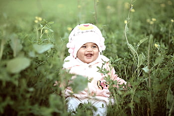 Cute baby in a warm hat laughing amidst green grass in a sunny field. HD wallpaper