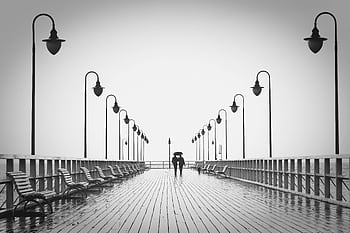 A couple holding umbrellas walks on a rainy boardwalk, embodying romance and tranquility. HD wallpaper