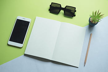 Flat lay of modern office essentials including smart, notepad, sunglasses, and plant. HD wallpaper